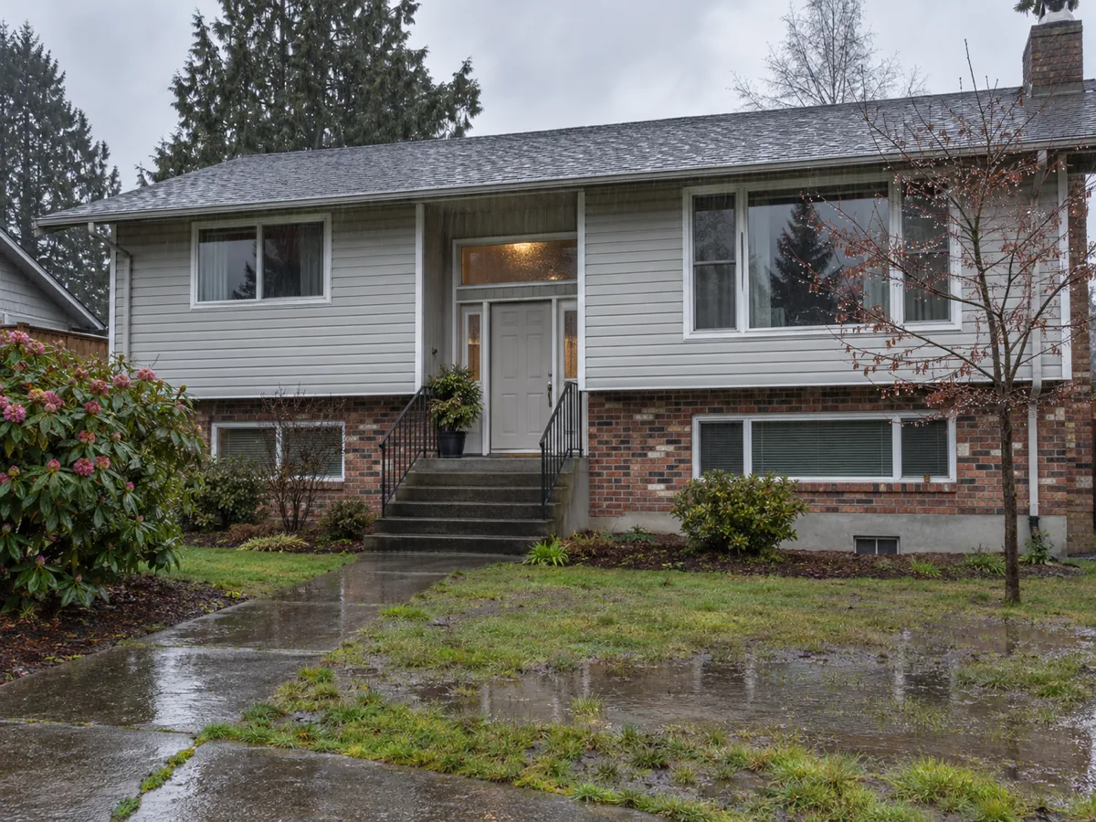 A 1980s split-entry home with vinyl siding and a crawl-space vent above a wet lawn in Puyallup, WA