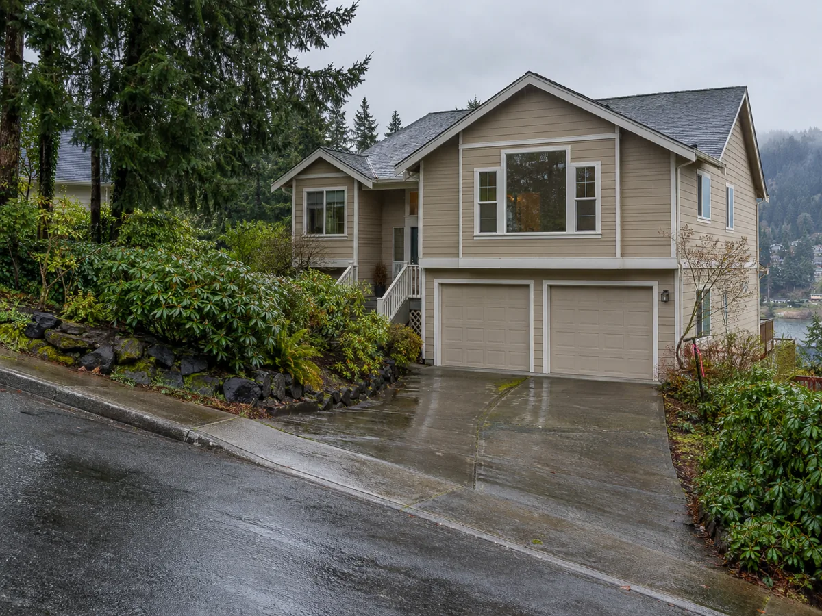 A late-1980s two-storey house on a fir-lined hillside street in the rain in Renton, WA